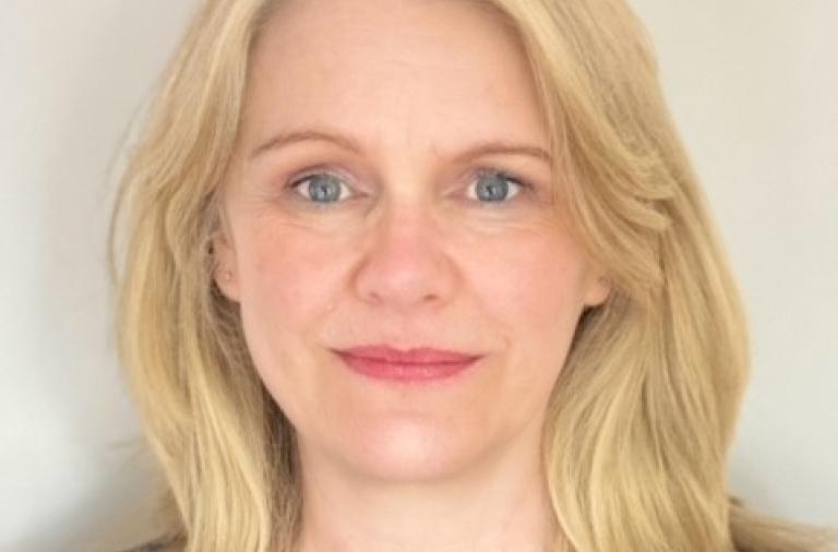 A smiling head shot of Karen Blagden who has long blonde hair, blue eyes and is wearing a black top